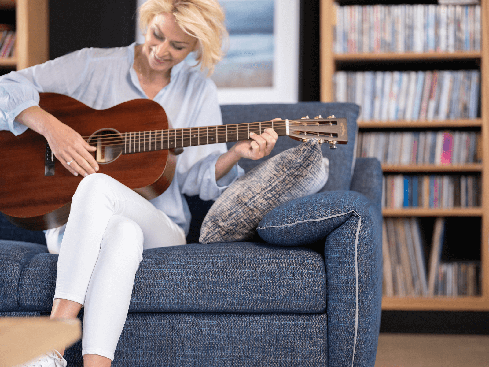 Gitarre spielende Frau auf einem blauen Schlafsofa